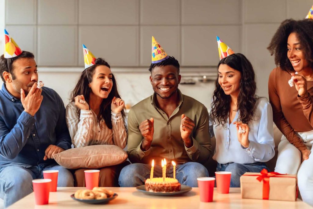 Group of friends celebrating a birthday with cake and party hats.