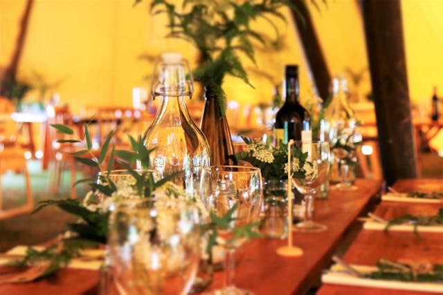 A decorated table with glass bottles, wine, candles, and floral arrangements in a warm, softly lit setting.