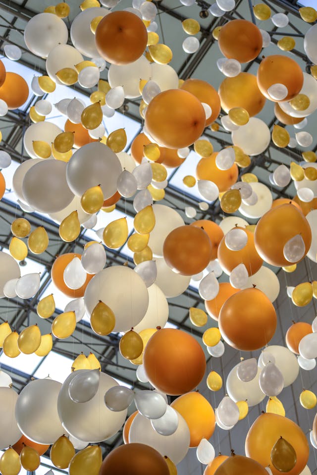 A ceiling installation featuring numerous orange, white, and yellow balloon-shaped decorations suspended from wires.