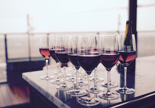 A row of wine glasses filled with red and rose wine on a table; a bottle of wine is placed next to the glasses.