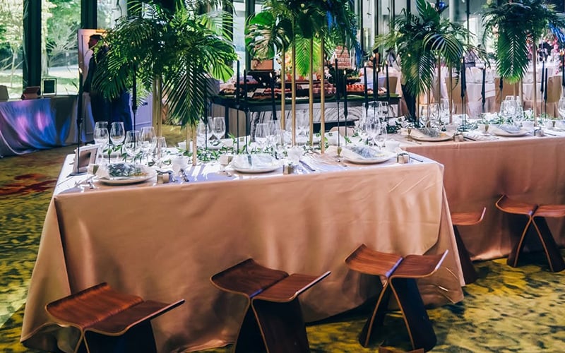 Elegant event dining tables with tropical plants and designer stools.